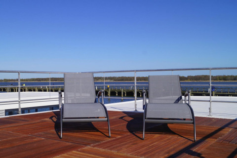 Zwei Liegestühle auf dem Sonnendeck eines Hausbootes mit Blick aufs Wasser unter blauem Himmel.
