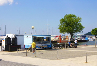 Harbor scene with food truck, benches, people and sailboats in the background at Ribnitz-Damgarten, Germany.