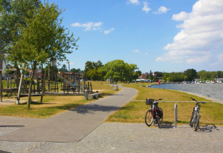 Senda junto al agua en Ribnitz-Damgarten con bicicletas, área de juegos, árboles y casas flotantes.