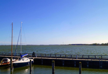 Blick von Hausboot 'Luisa' in Ribnitz-Damgarten, Deutschland, auf ruhigen See mit Segelbooten und Pier.
