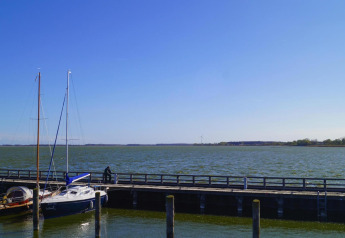 Blick von Hausboot 'Luisa' in Ribnitz-Damgarten, Deutschland, auf ruhigen See mit Segelbooten und Pier.