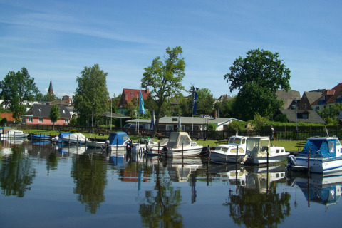 Péniches et petits bateaux amarrés dans le port calme de Ribnitz-Damgarten, entourés de maisons et d’arbres.