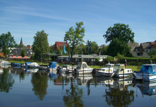 Péniches et petits bateaux amarrés dans le port calme de Ribnitz-Damgarten, entourés de maisons et d’arbres.