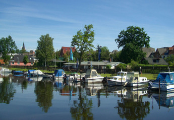 Casa flotante y barcos atracados en el puerto de Ribnitz-Damgarten, Alemania, con casas y árboles alrededor.