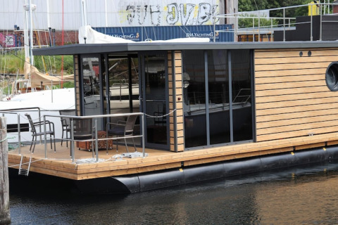 Houseboat moderno ‘Leni’ con pannelli in legno e porte a vetro ormeggiato in Germania, terrazza visibile.