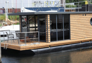 Houseboat moderno ‘Leni’ con pannelli in legno e porte a vetro ormeggiato in Germania, terrazza visibile.
