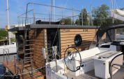 Moderne woonboot genaamd Leni aangemeerd in Duitsland met houten bekleding en rond patrijspoort raam.