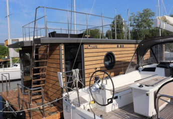 Moderne woonboot genaamd Leni aangemeerd in Duitsland met houten bekleding en rond patrijspoort raam.