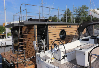 Casa flotante moderna llamada Leni amarrada en Alemania con fachada de madera y ventana circular.