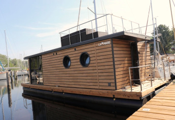 Moderne woonboot genaamd Houseboat «Leni» in een Duitse jachthaven, met houten bekleding en ronde ramen.