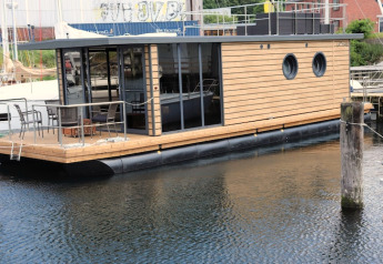 Moderne husbåd ved kajen i Tyskland, Houseboat «Leni» med træfacade og store runde vinduer.