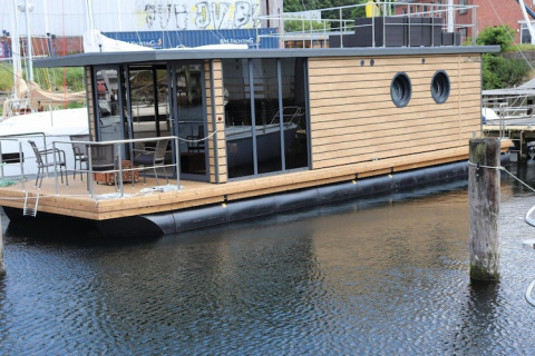 Moderna houseboat «Leni» in legno con oblò tondi, attraccata a un molo in Germania.
