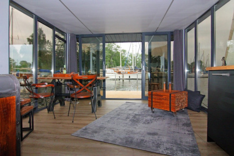 Indvendig udsigt fra Houseboat «Leni» i Tyskland med store vinduer, borde og udsigt til havnen.