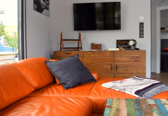 Moderne woonkamer op woonboot 'Leni' in Duitsland met oranje bank, houten kast en televisie.