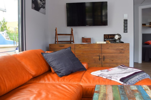 Soggiorno moderno sulla houseboat «Leni» in Germania con divano arancione, TV e coperta.