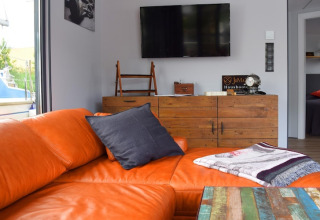 Modern living room on Houseboat 'Leni' in Germany with orange sofa, TV, rustic cabinet and blanket.