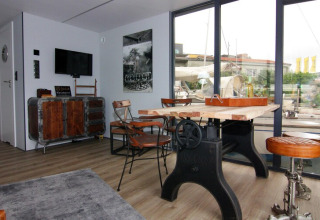 Zona giorno dell'houseboat 'Leni' in Germania con arredi industriali e grandi finestre sul porto.