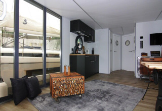 Modern living area on houseboat 'Leni' in Germany featuring large windows with a sailboat view outside.