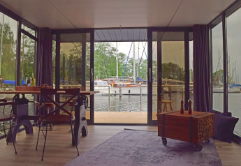 Udsigt fra stuen på husbåden 'Leni' i Tyskland med panorama vinduer over havnen og sejlbåde.