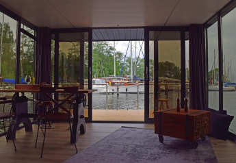 Binnenzicht vanuit woonboot ‘Leni’ in Duitsland, grote ramen met zicht op jachthaven en zeilboten.