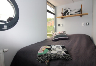 Slaapkamer op woonboot «Leni» in Duitsland met bed, kussens en uitzicht door een groot raam.