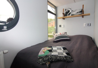 Chambre sur la péniche «Leni» en Allemagne avec un lit simple, coussins et grande fenêtre lumineuse.