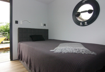 Chambre moderne sur la péniche « Leni » en Allemagne, avec hublot rond et couvre-lit foncé.