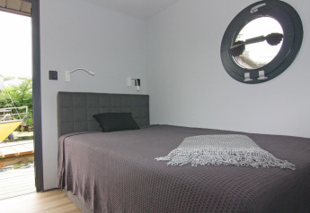 Chambre lumineuse avec lit double, hublot rond et vue sur terrasse sur la péniche Leni en Allemagne.