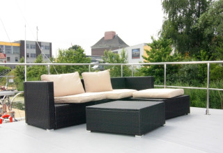 Outdoor seating area with dark rattan sofa and light cushions on the deck of Houseboat “Leni” in Germany.