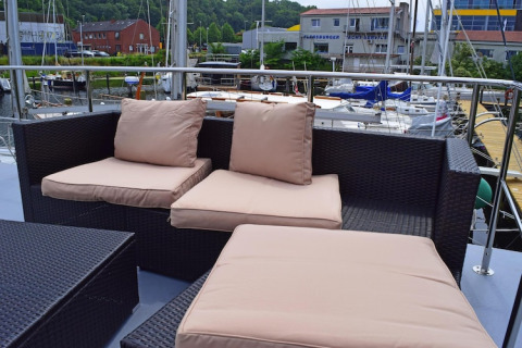 Area salotto esterna con cuscini beige sul ponte della houseboat Leni in Germania, vista porto turistico.