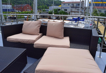 Buiten zetelhoek met beige kussens op het dek van de houseboat Leni in Duitsland, met jachthaven achteraan.