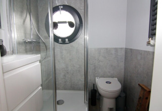 Baño moderno en una casa flotante con ventana redonda, ducha, inodoro y tocador, Houseboat «Leni», Alemania.