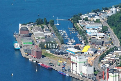 Luftfoto af husbåde og marina ved havnen i Tyskland med både, bygninger og lagerområder.