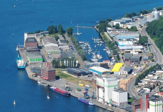 Luftfoto af husbåde og marina ved havnen i Tyskland med både, bygninger og lagerområder.