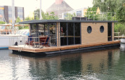 Et moderne husbåd kaldet Houseboat «Lina» i Tyskland, fortøjet ved en rolig havn en sommerdag.