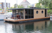 Et moderne husbåd kaldet Houseboat «Lina» i Tyskland, fortøjet ved en rolig havn en sommerdag.