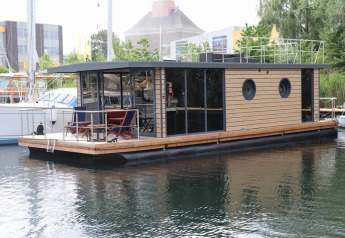 Casa flotante moderna llamada Houseboat «Lina» en Alemania, amarrada en un puerto tranquilo.