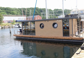 Houseboat «Lina» docked at a marina in Germany, surrounded by lush green hills and nearby boats.