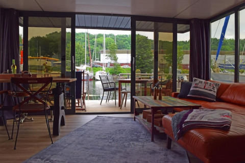 Living room on Houseboat ‘Lina’ in Germany, featuring large glass doors, marina view, and cozy decor.