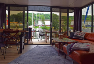 Living room on Houseboat ‘Lina’ in Germany, featuring large glass doors, marina view, and cozy decor.