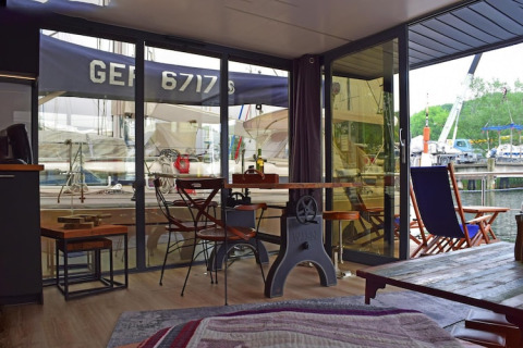 Interior view from Houseboat Lina in Germany with dining table, chairs, and a harbor view outside.