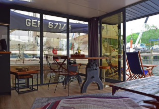 Interior view from Houseboat Lina in Germany with dining table, chairs, and a harbor view outside.