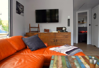 Woonkamer op woonboot 'Lina' in Duitsland met oranje bank, kleurrijke tafel en houten dressoir.