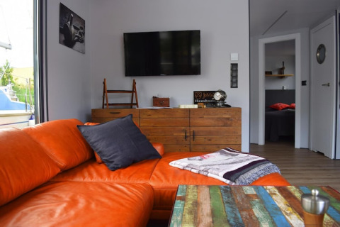 Living area on houseboat 'Lina' in Germany with orange sofa, colorful table, and rustic wooden dresser.
