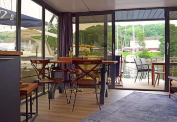 Woonruimte op woonboot «Lina» in Duitsland met eettafel, stoelen en uitzicht op haven door glazen deuren.
