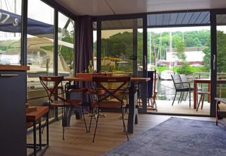 Living area on houseboat «Lina» in Germany with dining table, chairs, and marina view through glass doors.