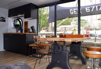 Interieur van houseboat Lina in Duitsland met een houten tafel, moderne keuken en uitzicht op de haven.