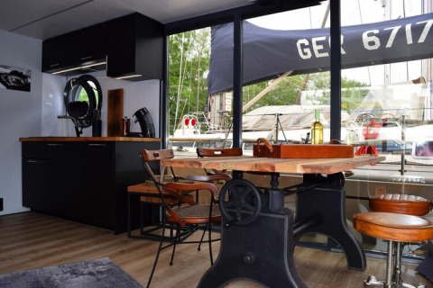 Interior of Houseboat Lina in Germany featuring a rustic table, modern kitchen area, and marina view.