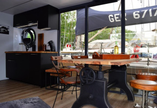 Interior of Houseboat Lina in Germany featuring a rustic table, modern kitchen area, and marina view.