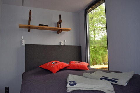 Bedroom on Houseboat Lina in Germany featuring a gray bed, shelf, open window, and red pillows.